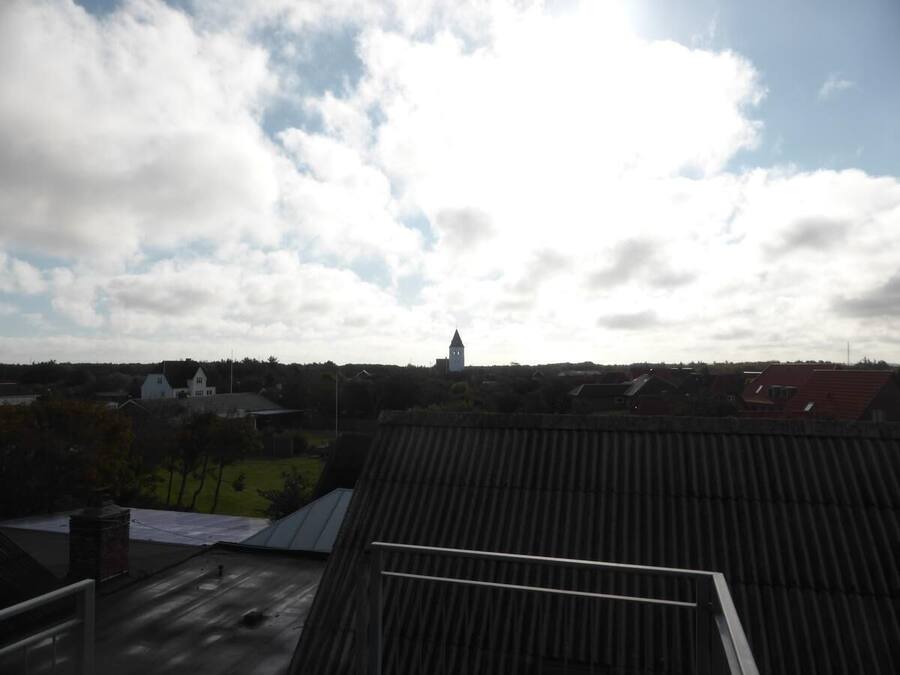 A view of a town with a prominent church tower, surrounded by residential houses and greenery.
