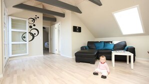 Un salón amplio con techo alto, un sofá de cuero negro, una mesa de centro blanca y un niño sentado en el suelo.