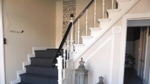Una escalera con peldaños de moqueta oscura y balaustres blancos, flanqueada por dos faroles ornamentales.