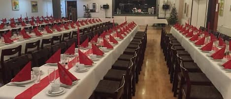 A banquet hall with long tables set for a formal event, featuring red napkins and white tablecloths.
