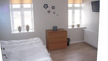 A bedroom with a bed, a wooden dresser, a radiator, and a window with curtains.
