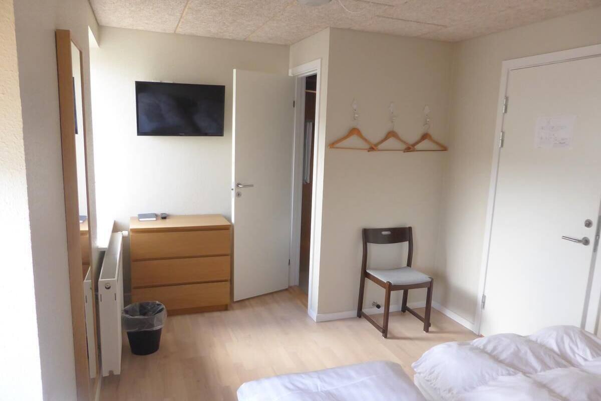 Ein Schlafzimmer mit einem Bett, einem Holzschrank, einem Sessel, einem Fernseher und einem Kleiderschrank.