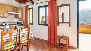 Um quarto aconchegante com teto de madeira, sala de jantar com cadeiras listradas, uma pequena mesa e vista para montanhas por uma porta de varanda.