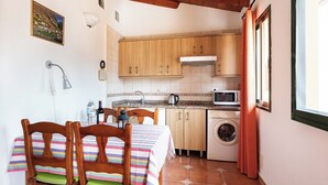 Uma cozinha compacta com armários de madeira, uma máquina de lavar e uma área de refeições com toalha de mesa listrada.