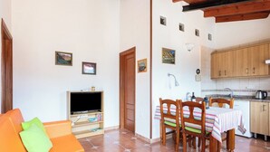 Uma sala de estar com um sofá laranja, uma televisão e uma área de jantar com mesa e cadeiras.