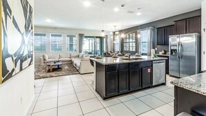 A modern kitchen with a central island, dark cabinets, stainless steel appliances, and a dining area with a sofa and coffee table. - Disney Retreat! Gameroom! Solterra Resort Near Theme Parks ! (Davenport)