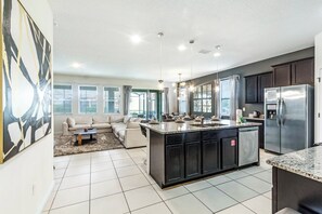 A modern kitchen with a central island, dark cabinets, stainless steel appliances, and a dining area with a sofa and coffee table.