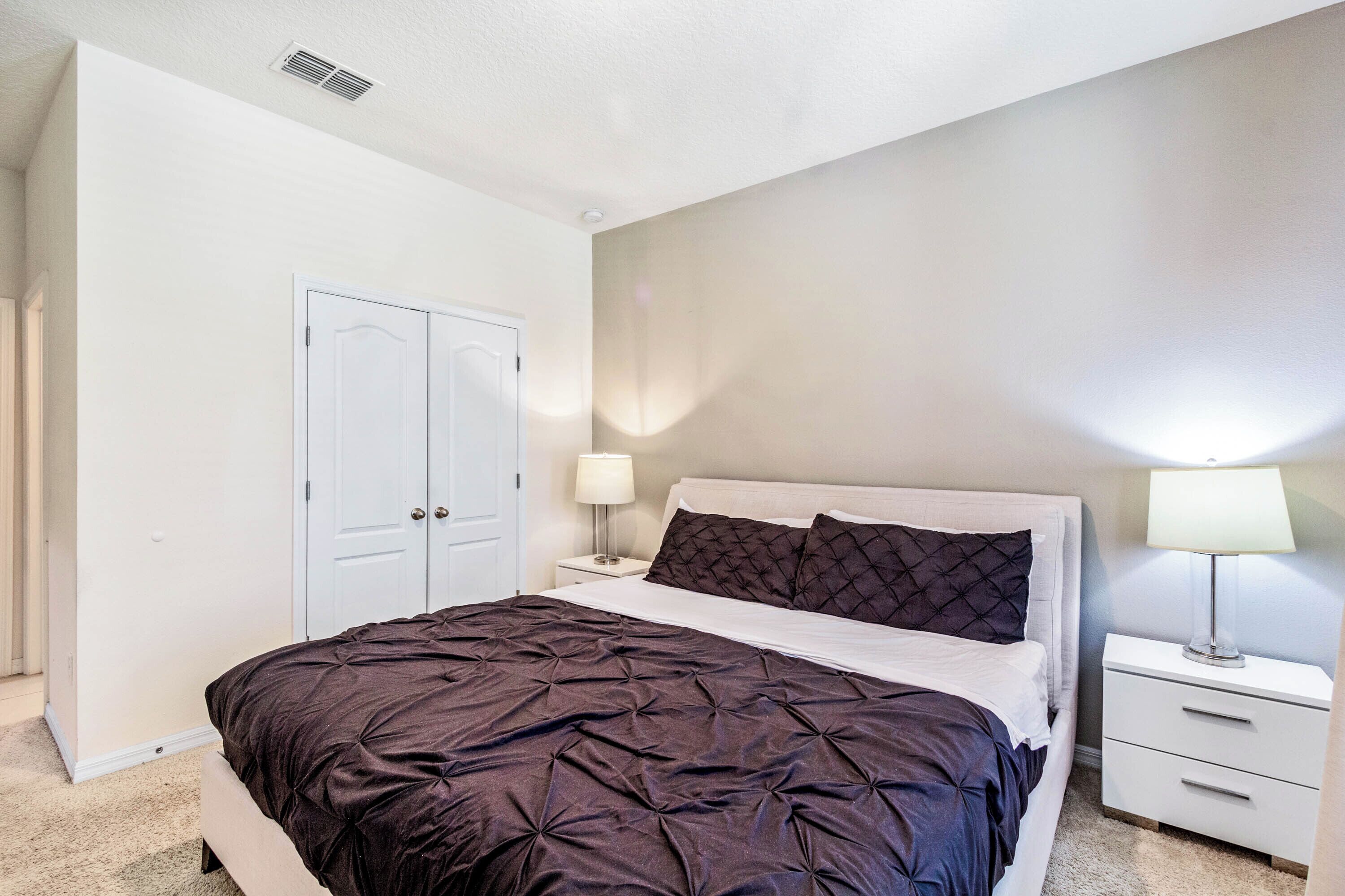 A bedroom with a large bed, a nightstand with a lamp, and a wardrobe.