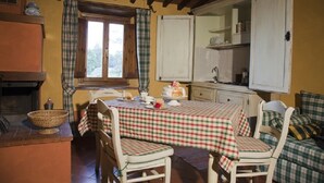 A cozy dining area with a checkered tablecloth, two chairs, a window with curtains, a kitchen area with cabinets, and a basket on the counter. - APARTMENT SANGIOVESE (Pontassieve)
