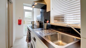 A modern kitchen with a stainless steel sink, black tiled backsplash, and a window with blinds.