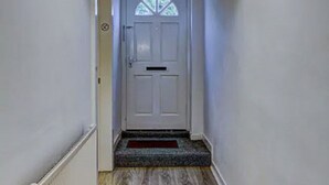 A narrow hallway with a white door at the end, a radiator on the left, and a wooden floor.