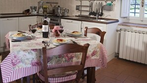 A rustic kitchen with wooden beams, white cabinets, and a dining table set with plates and wine glasses. - APARTMENT DELUXE (Pontassieve)