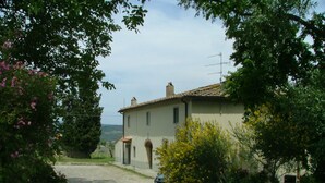 A rural house with a dirt driveway, surrounded by greenery and flowering plants. - APARTMENT DELUXE (Pontassieve)