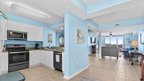 A spacious kitchen with white cabinets, a microwave, and an oven. There is a dining area with a gray sofa and a table.