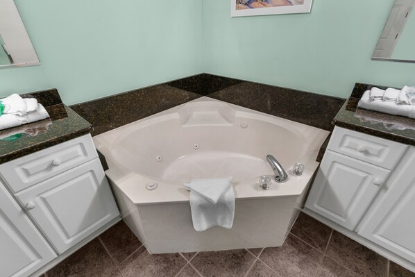 A bathroom with a freestanding bathtub, white cabinetry, and a granite countertop.