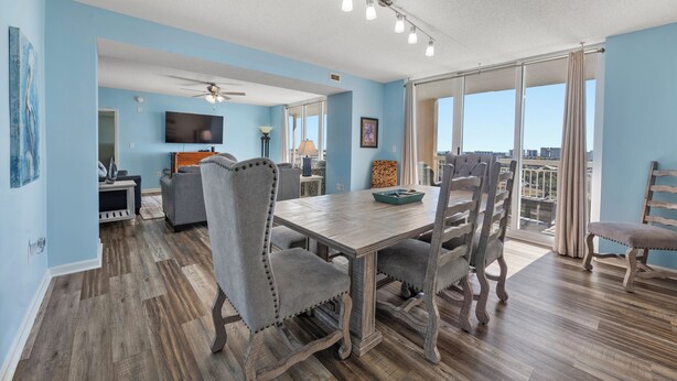 A dining area with a wooden table and chairs, a television, and a city view through large windows.