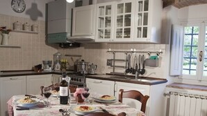 Une cuisine rustique avec des poutres en bois, des armoires blanches et une table à manger dressée pour deux personnes, recouverte de nappes à motifs floraux.