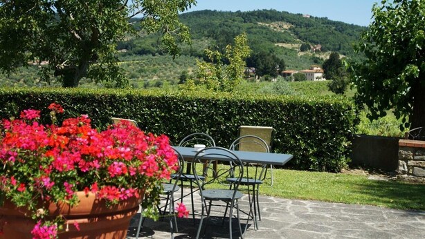 Une terrasse extérieure avec une table et des chaises, entourée de verdure et offrant une vue sur des collines ondoyantes.