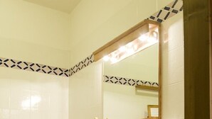 Une salle de bain avec un grand lavabo, un bidet et un miroir avec éclairage intégré. Des serviettes sont suspendues sur un porte-serviettes et une étagère en bois se trouve au-dessus du lavabo.