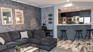 A modern living room with a sectional sofa, a glass coffee table, and a kitchen area with a bar and high-end appliances. - 2BR Modern Scottsdale Condo W/  Heated Pool, Hot Tub, Kg Bed, Gym, & Fast WiFi (Scottsdale)