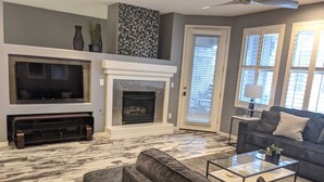 A living room with a fireplace, a television, a sofa, and a coffee table. - 2BR Modern Scottsdale Condo W/  Heated Pool, Hot Tub, Kg Bed, Gym, & Fast WiFi (Scottsdale)