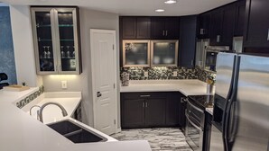 A modern kitchen with dark cabinets, a stainless steel refrigerator, and a tiled backsplash. - 2BR Modern Scottsdale Condo W/  Heated Pool, Hot Tub, Kg Bed, Gym, & Fast WiFi (Scottsdale)