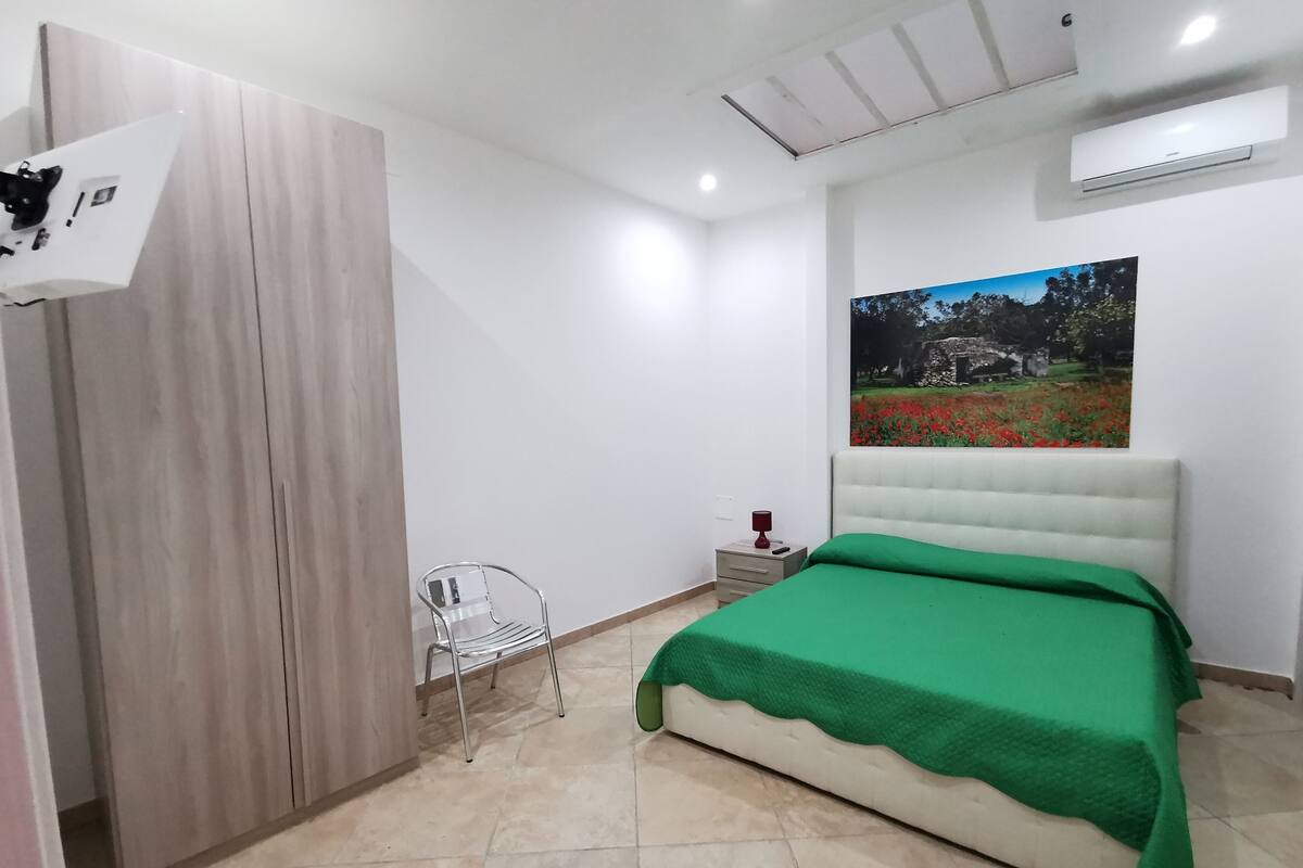 A bedroom with a bed, a wardrobe, a chair, a nightstand, and a wall-mounted air conditioner.