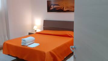 A hotel room with a bed covered in orange bedding, a nightstand with a lamp, and a painting on the wall.