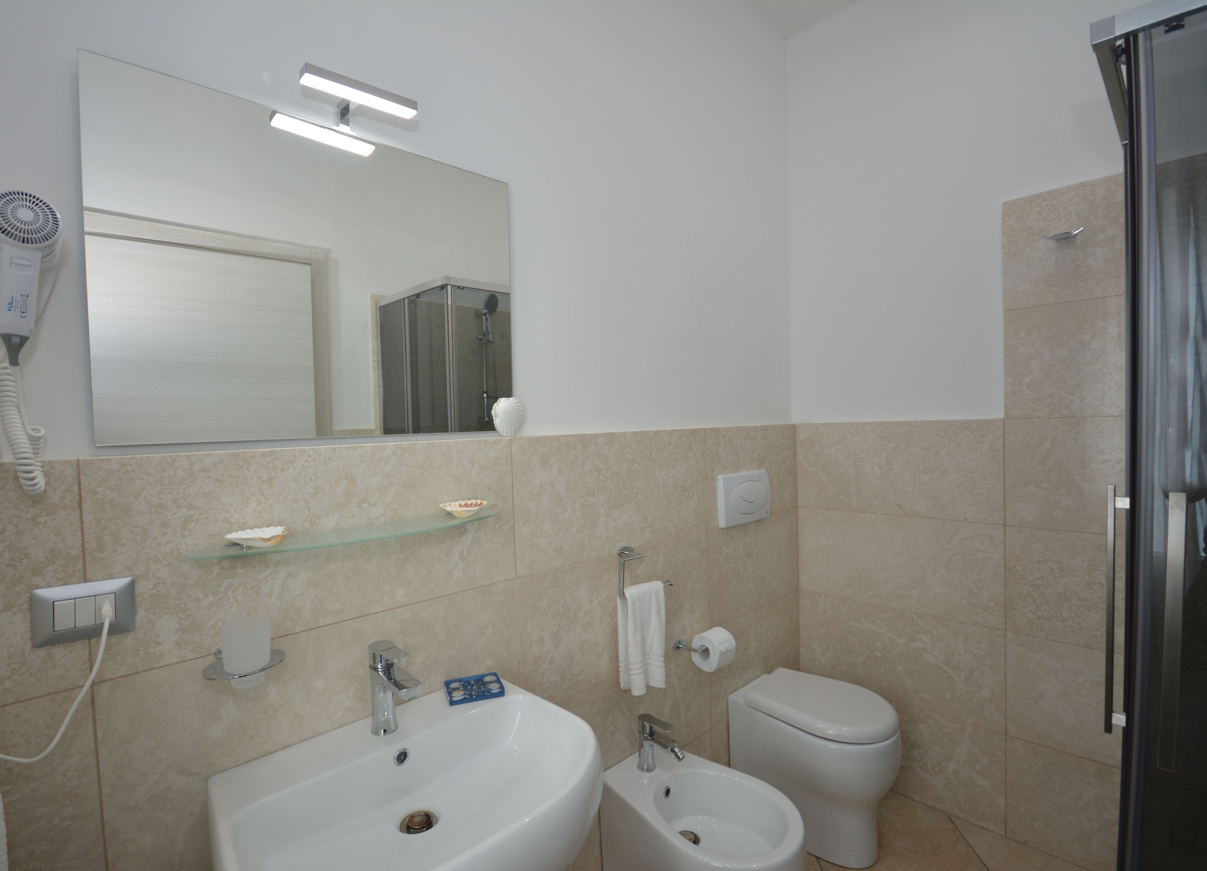 A modern bathroom with a sink, bidet, toilet, and a glass shelf.