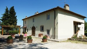 A two-story building with a tiled roof, a wooden door, and a small porch with outdoor seating. - VILLA SOURROUNDED WITH VINEYARDS - BORGO CASANOVA (Pontassieve)