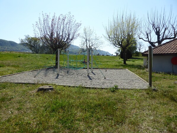 A playground with a net structure, surrounded by grass and trees.