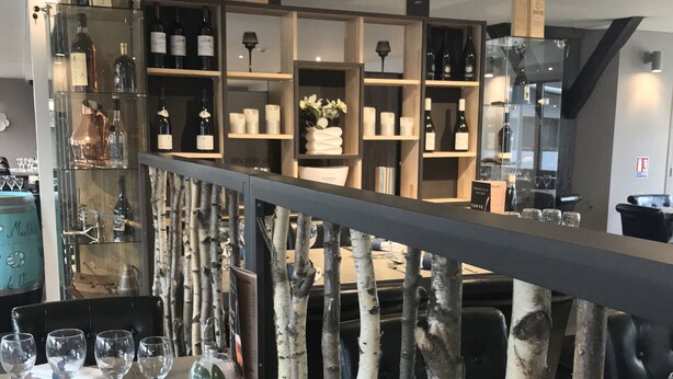 Interior de un restaurante con una larga mesa de comedor, sillas y una barrera decorativa en forma de árbol.
