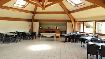 A spacious dining area with multiple tables and chairs, wooden beams on the ceiling, and skylights allowing natural light.