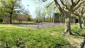Un parque con cancha de tenis, árboles y zona verde.