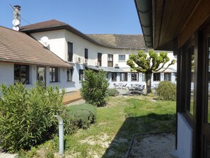 Un patio con un edificio que tiene varias ventanas, un árbol y mobiliario exterior.
