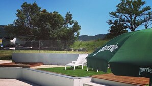 Un patio con una sombrilla verde, sillas blancas de descanso y un muro de piedra.