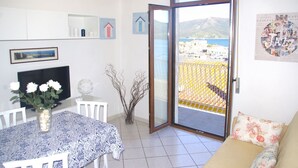 A room with a dining table, chairs, a sofa, a TV, a balcony with a view of the sea, and a poster on the wall. - Cosmopolis (Portoferraio)