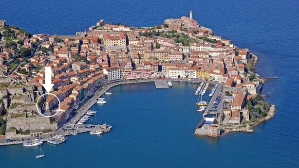 An aerial view of a coastal town with a historic fort, a marina, and a prominent lighthouse. - Cosmopolis (Portoferraio)