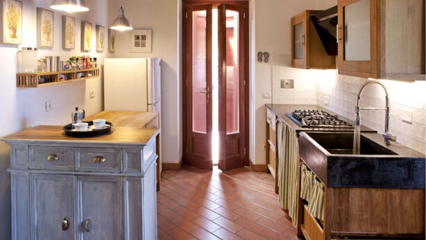 A kitchen with a wooden countertop, a stove, and a sink. There are cabinets and a door leading to another room. - Cottage Vittoria (Portoferraio)