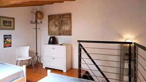A bedroom with a wooden ceiling, a white dresser, a globe artwork, a hat on a stand, and a staircase with a metal railing. - Cottage Vittoria (Portoferraio)