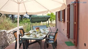 An outdoor dining area with a table set for four, surrounded by chairs, under a large umbrella. - Cottage Vittoria (Portoferraio)