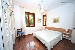 A bedroom with a bed, a chair, a ceiling fan, and a window. - Villa Enfola (Portoferraio)