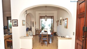 A dining area with a long table, chairs, and a view through an archway to the outside.