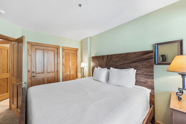 A hotel room with a large bed, wooden wardrobe, and a nightstand with a lamp.