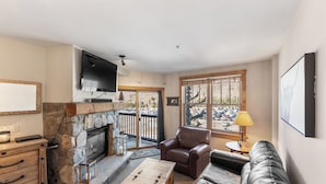 A cozy living room with a stone fireplace, leather sofa, and a television mounted on the wall.