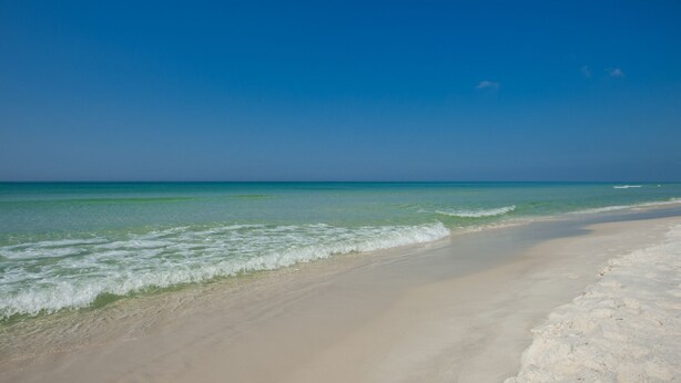A beach with clear blue water and a sandy shore.