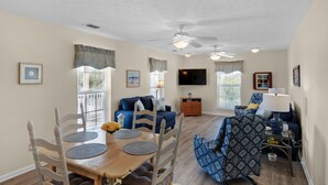 A spacious living room with a dining area, ceiling fans, and a flat-screen TV.