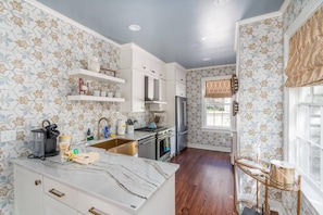 A kitchen with white cabinets, a marble countertop, and a stainless steel refrigerator. - Historic Charm | The Bee & Blossom (Charleston)