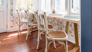 A dining area with a wooden table and chairs, patterned wallpaper, and a window with a view. - Historic Charm | The Bee & Blossom (Charleston)
