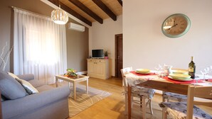 Ein Wohnzimmer mit einer Couch, einem Esstisch für zwei Personen, einem Fernseher und einer Wanduhr.